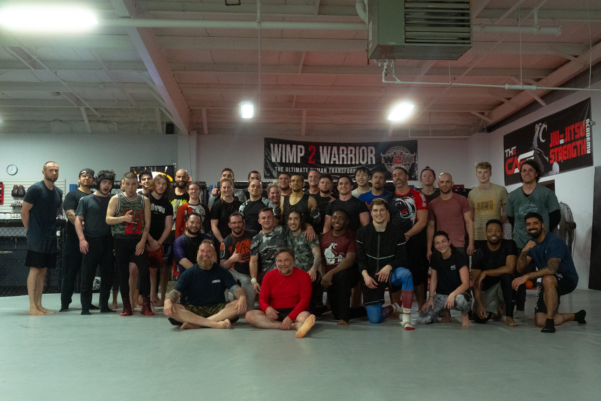 A full class of around forty members posed together on the mat under the gym banners at TRITAC Training Center