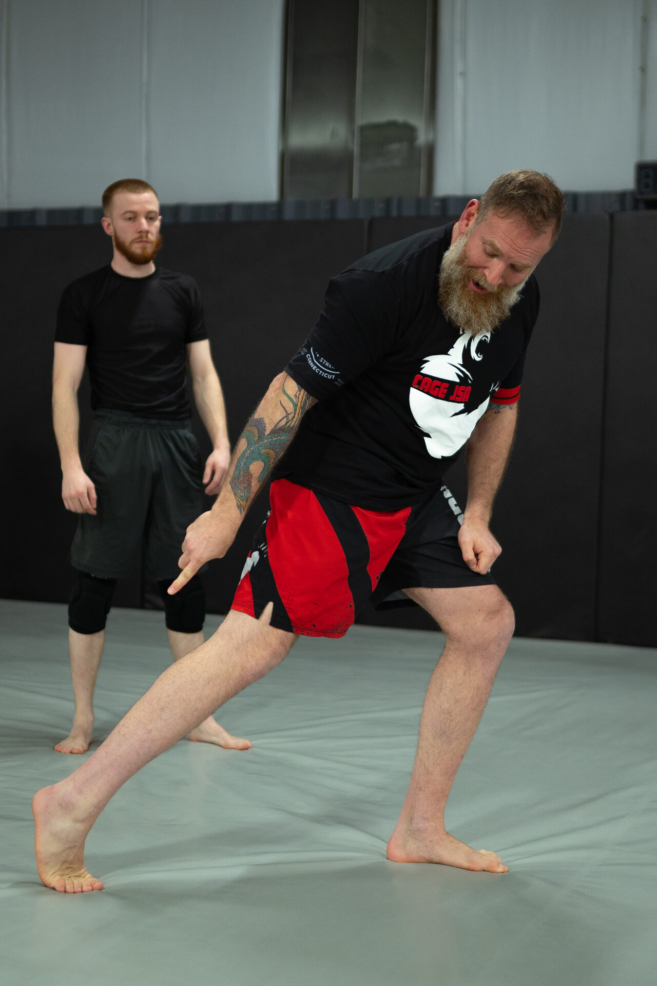 Matt Bryers in a TRITAC shirt, low in a stance mid-demonstration while a student watches