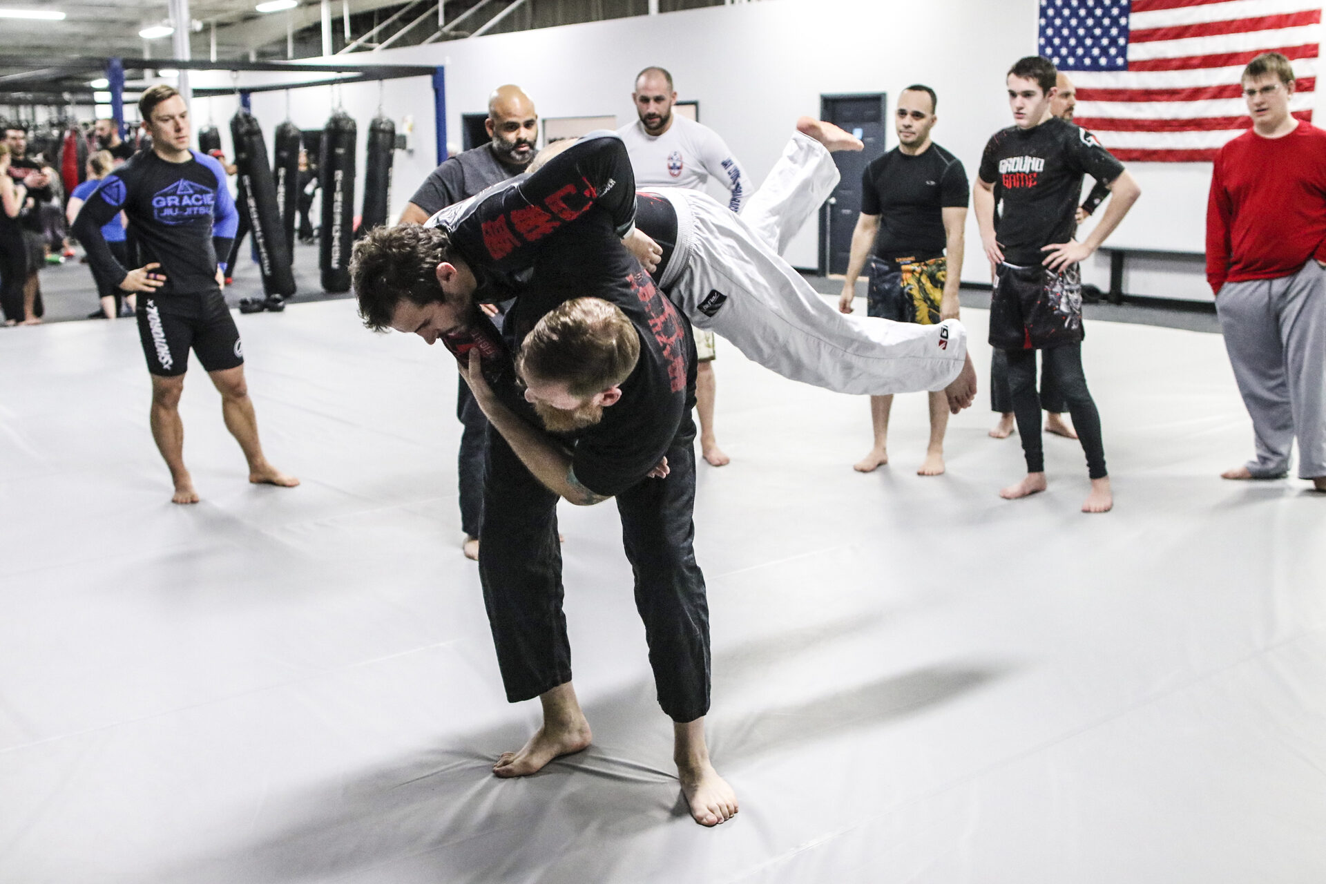 A coach demonstrating a technique to a standing class on the mat at TRITAC Training Center