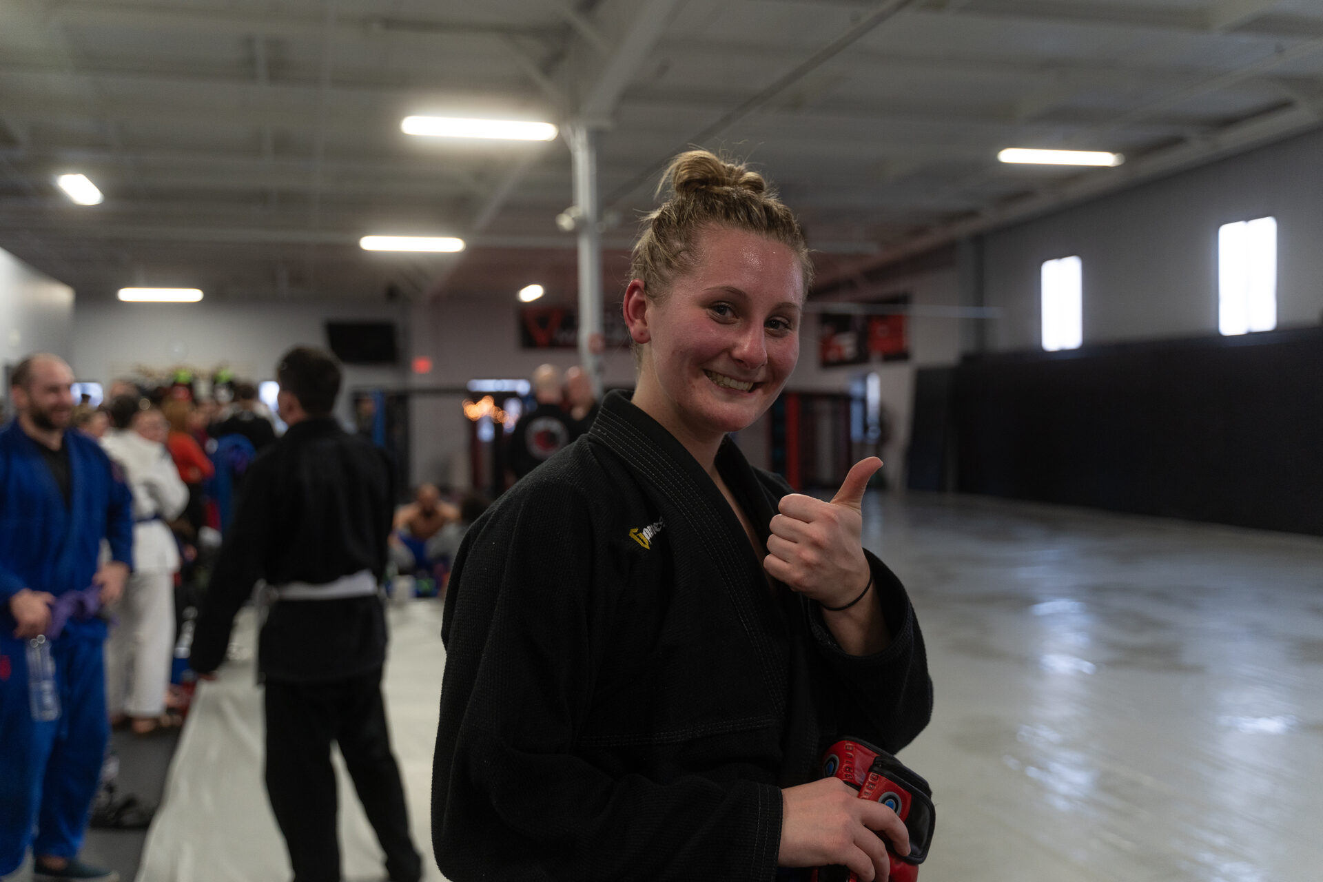 A member in a black gi before class, the gym floor and other members behind her