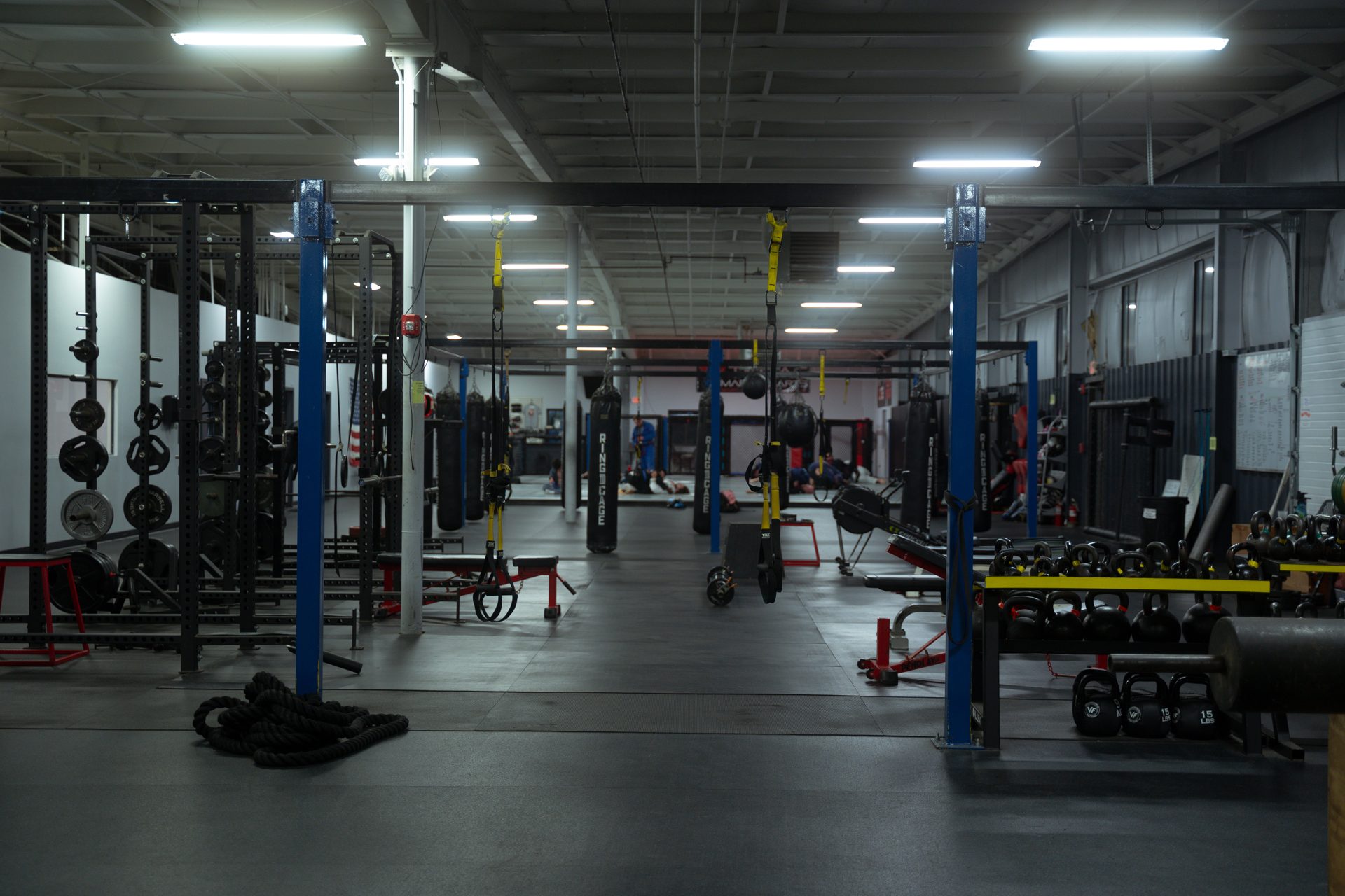The training floor at TRITAC Training Center: squat racks and kettlebells in the foreground, the heavy bag row and the cage behind